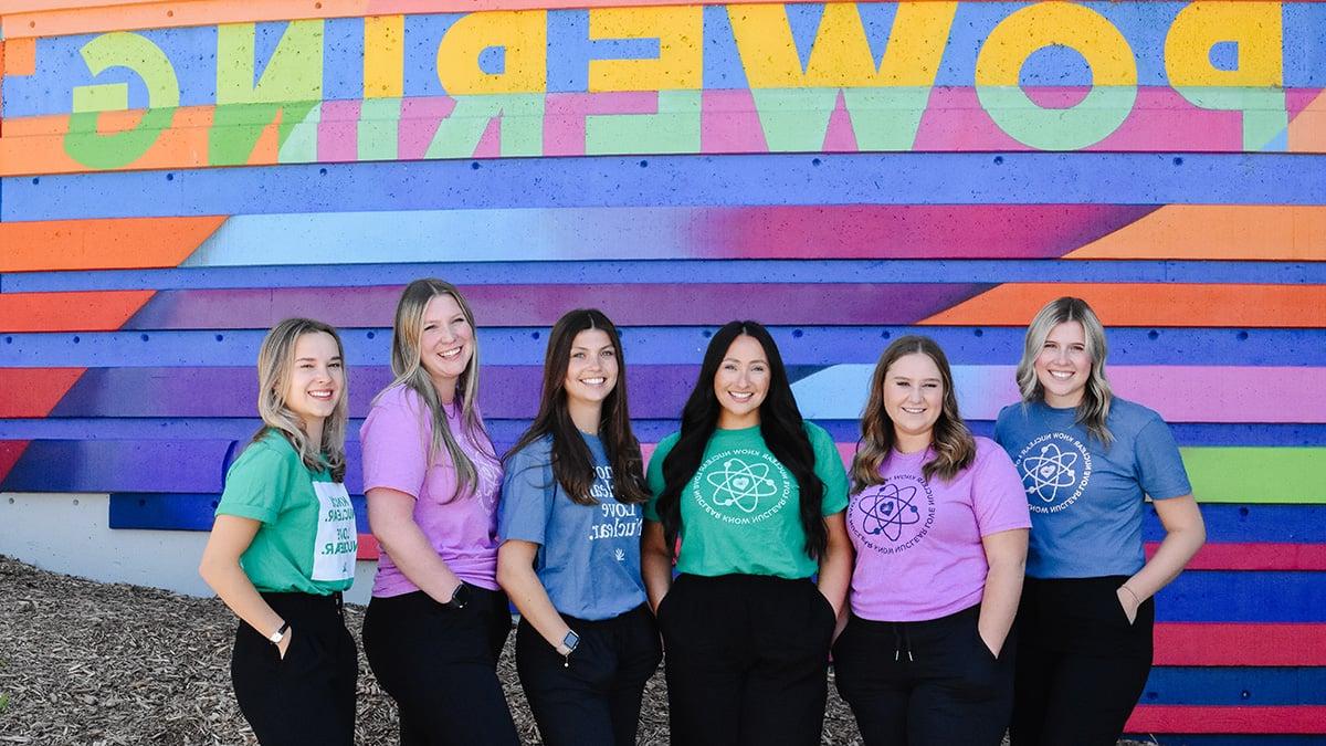 Group of six female students in front of ‘Powering’ sign. 