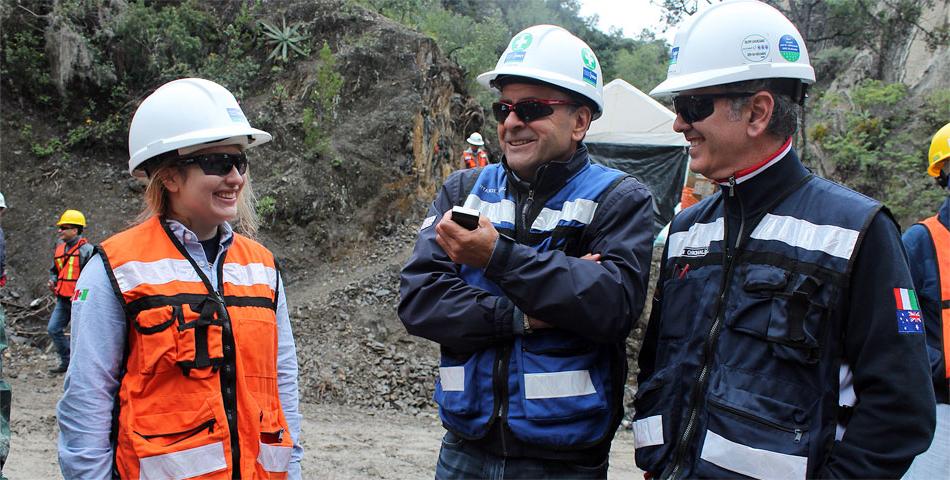 Three safety-conscious individuals in hard hats and sunglasses converse at a construction site.